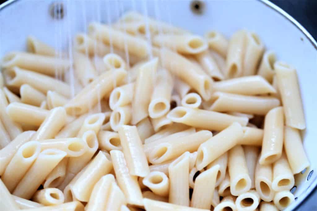 rinsing cooked pasta in a colander under cold water