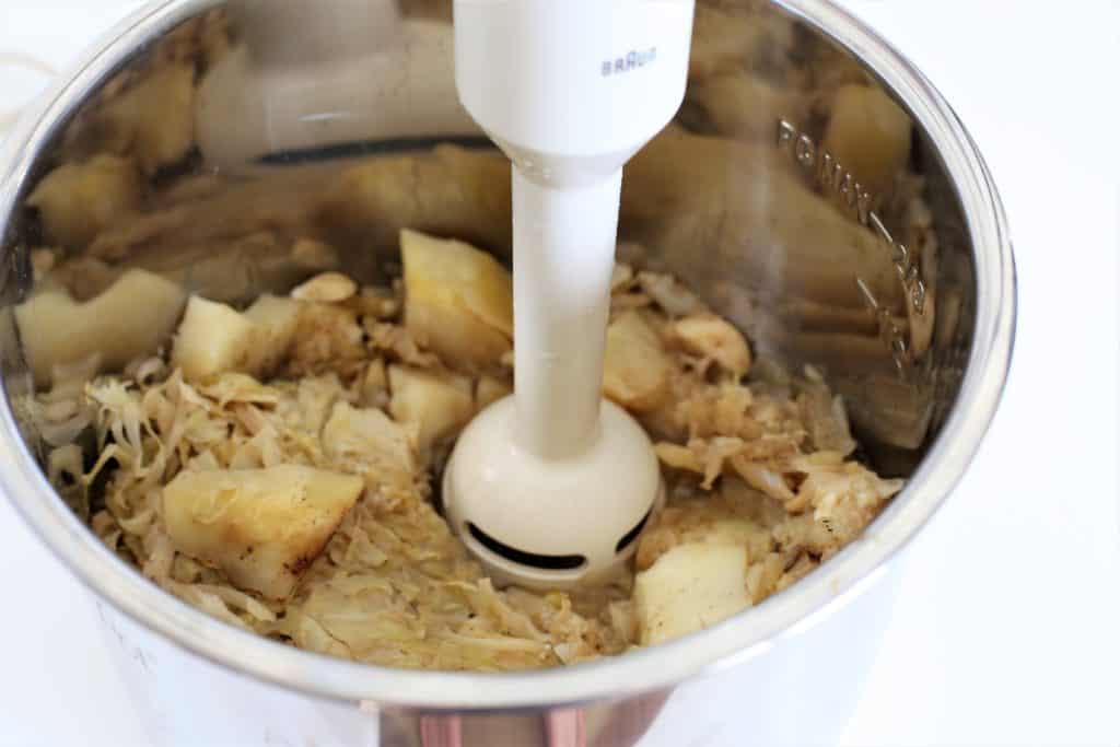 potatoes and cabbage being blended with a small hand blender