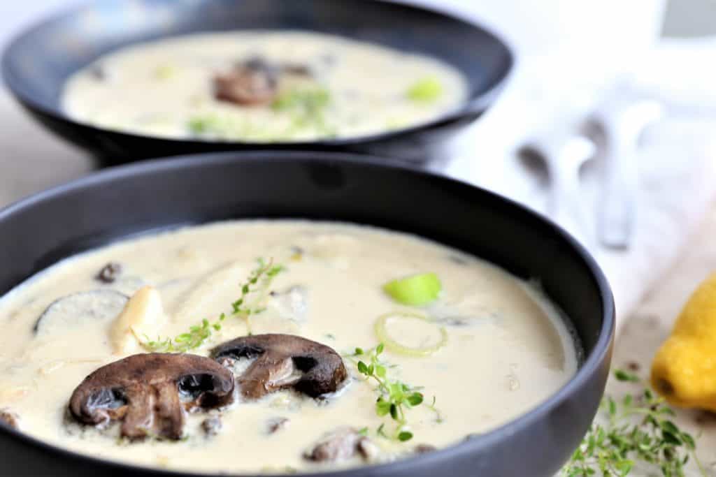 two servings of cream of mushroom tarragon soup in black bowls