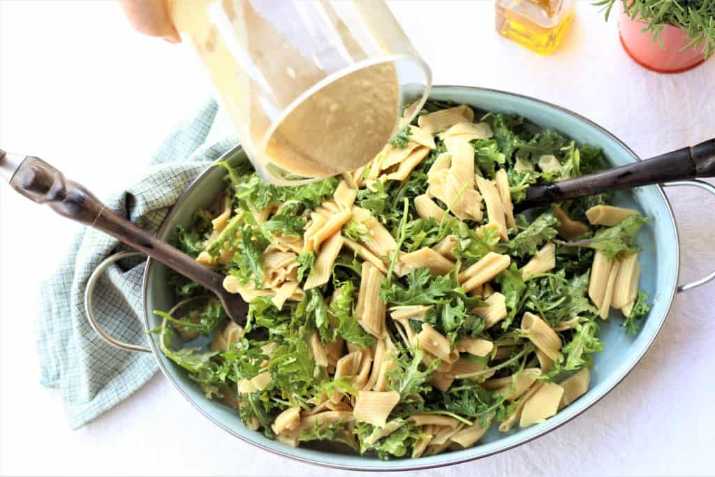 pouring alfredo sauce over pasta and kale