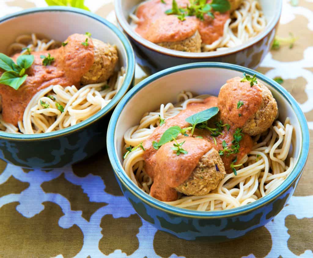 three servings of vegan spaghetti and meatballs in blue bowls. 