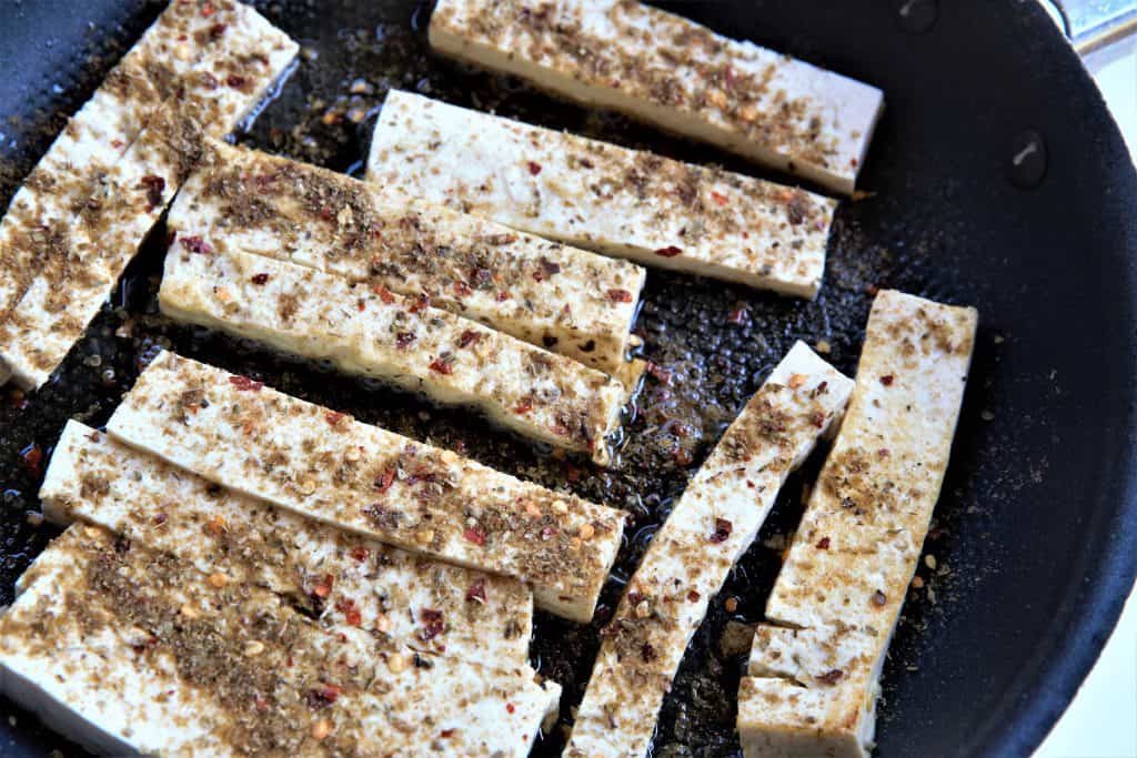 sliced tofu with seasonings cooking in a pan