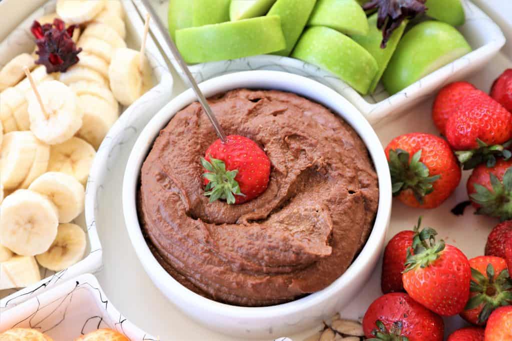 strawberry being dipped into chocolate hummus in a serving platter