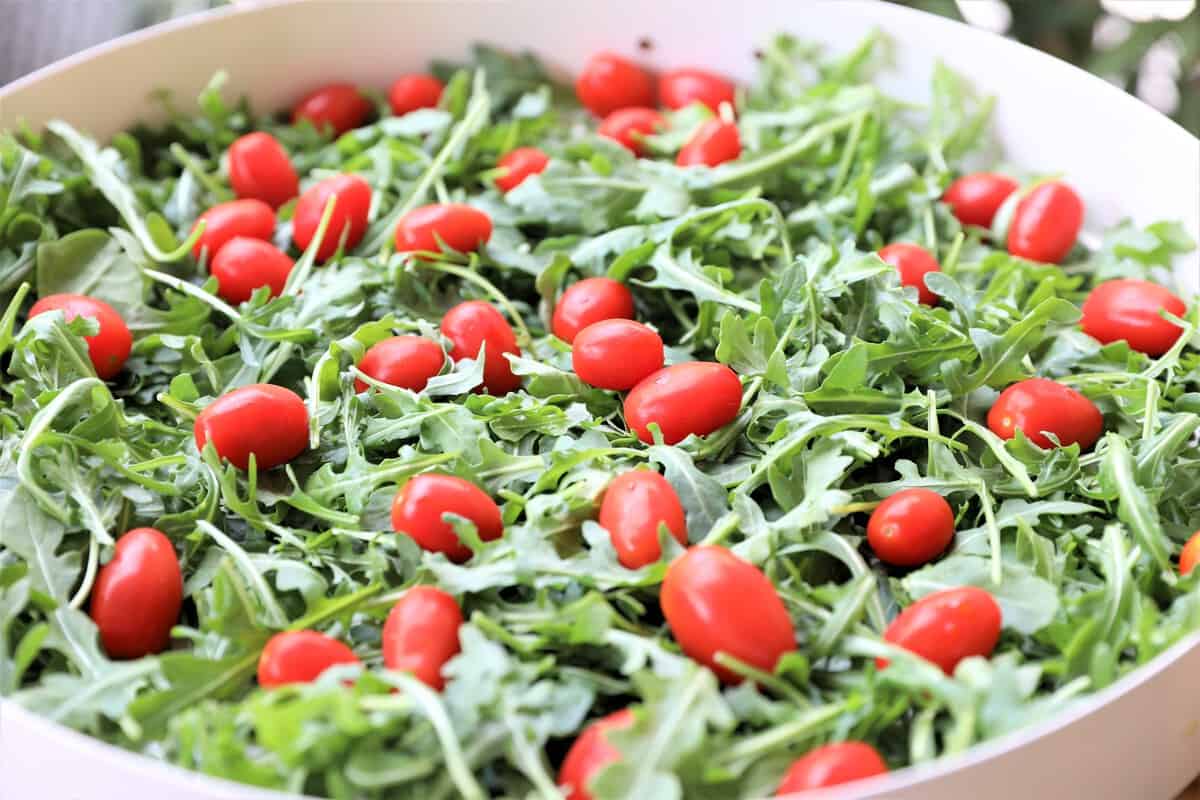 arugula salad topped with cherry tomatoes in a large white serving bowl
