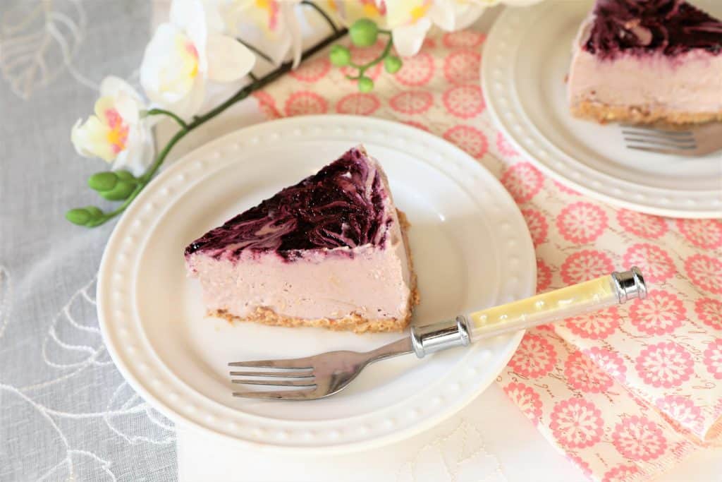 two slices of vegan berry cheesecake on white plates with a fork