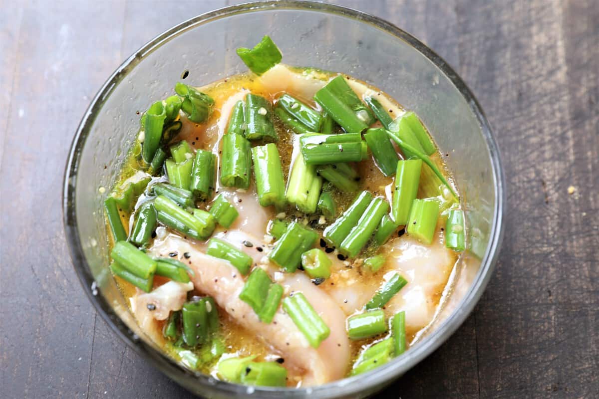 chicken, marinade, and green onions in a bowl